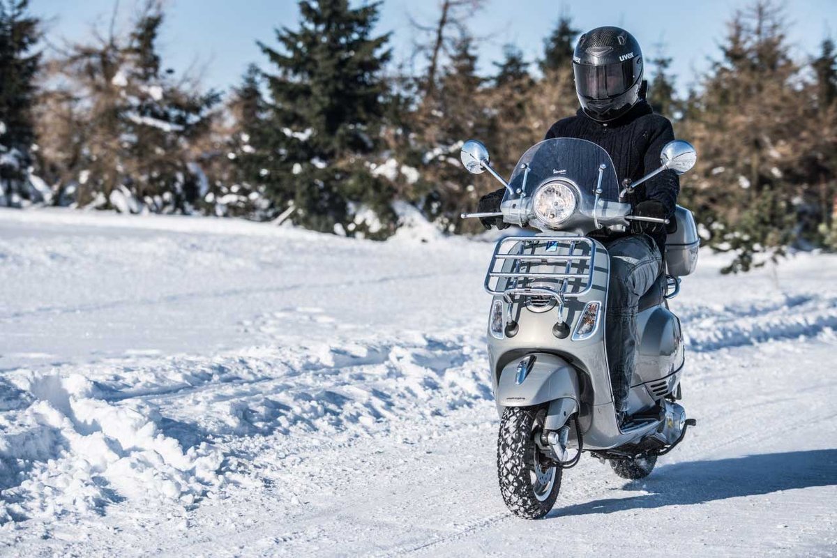 Conducteur roulant en scooter sur une route enneigée en hiver
