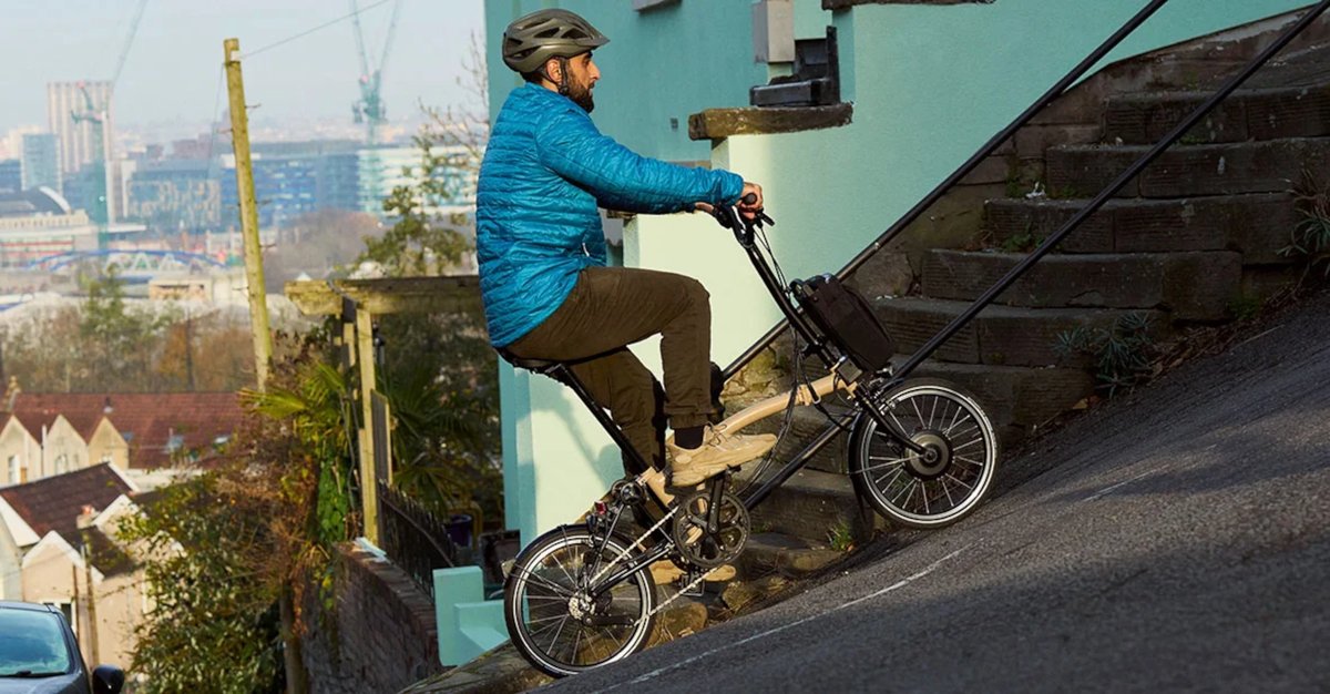 Cycliste sur un vélo électrique pliant Brompton grimpant une rue très escarpée en ville.