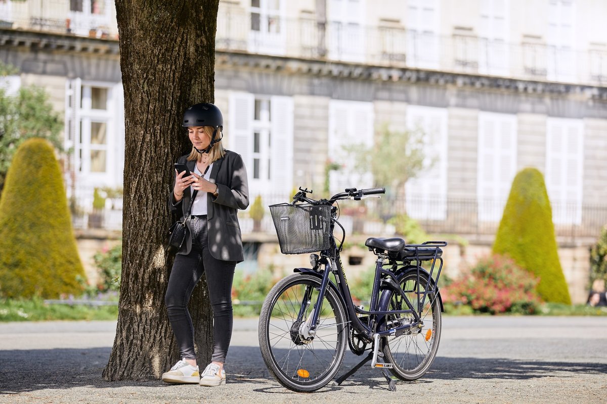 Cycliste connectée utilisant son smartphone à côté d’un vélo électrique Velco à Nantes.