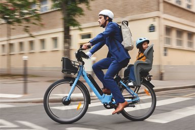 Homme en costume sur un vélo électrique Véligo avec un siège enfant en Île-de-France