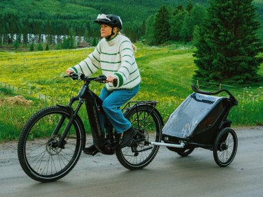 Cannondale Moterra EQ 2025 : femme roulant en campagne avec un VTC électrique tout suspendu et une remorque enfant