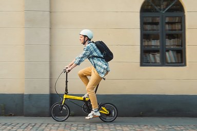 Cycliste en Dahon pliant jaune en ville, casque et sac à dos