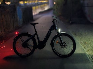 Vélo électrique O2feel Duma avec éclairages avant et arrière allumés sur une voie urbaine de nuit.
