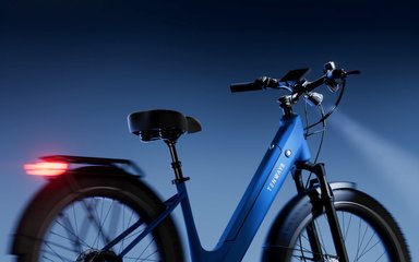 Vélo électrique Tenways Wayfarer bleu avec cadre bas, éclairage avant et feu arrière allumé, typé cruiser