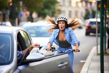 Cycliste passant à côté d'une voiture avec portière ouverte en ville, illustrant le risque de dooring