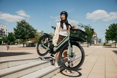 Femme portant un vélo électrique Canyon vert sur des marches en ville.