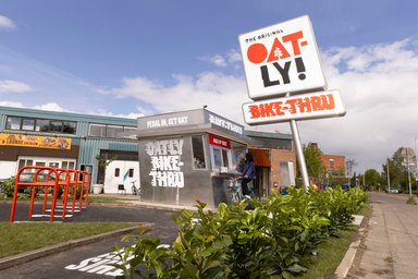 Cycliste commandant au comptoir du stand Oatly Bike-Thru à Amsterdam avec son enseigne distinctive.