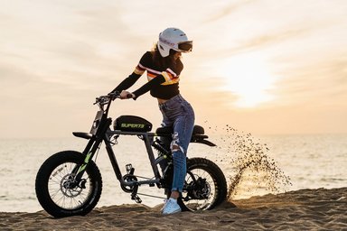 Une femme pilote un vélo électrique Super73 RX puissant sur une plage de sable au coucher du soleil.