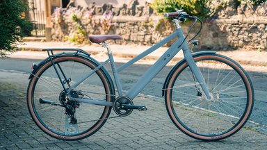 Temple Electric II, vélo électrique urbain gris bleu avec cadre trapèze et pneus à flancs marron.