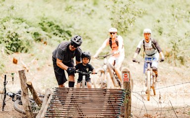 Un adulte aide un jeune enfant à vélo à franchir un passage sur un sentier de VTT forestier.