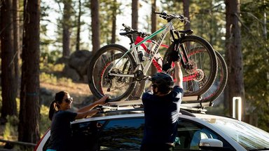 Deux cyclistes chargent des VTT Specialized sur les barres de toit d'une voiture en forêt