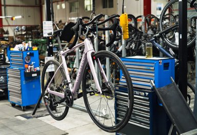 Vélo de route rose pâle suspendu dans un atelier de réparation Decathlon avec outils et autres vélos en arrière-plan