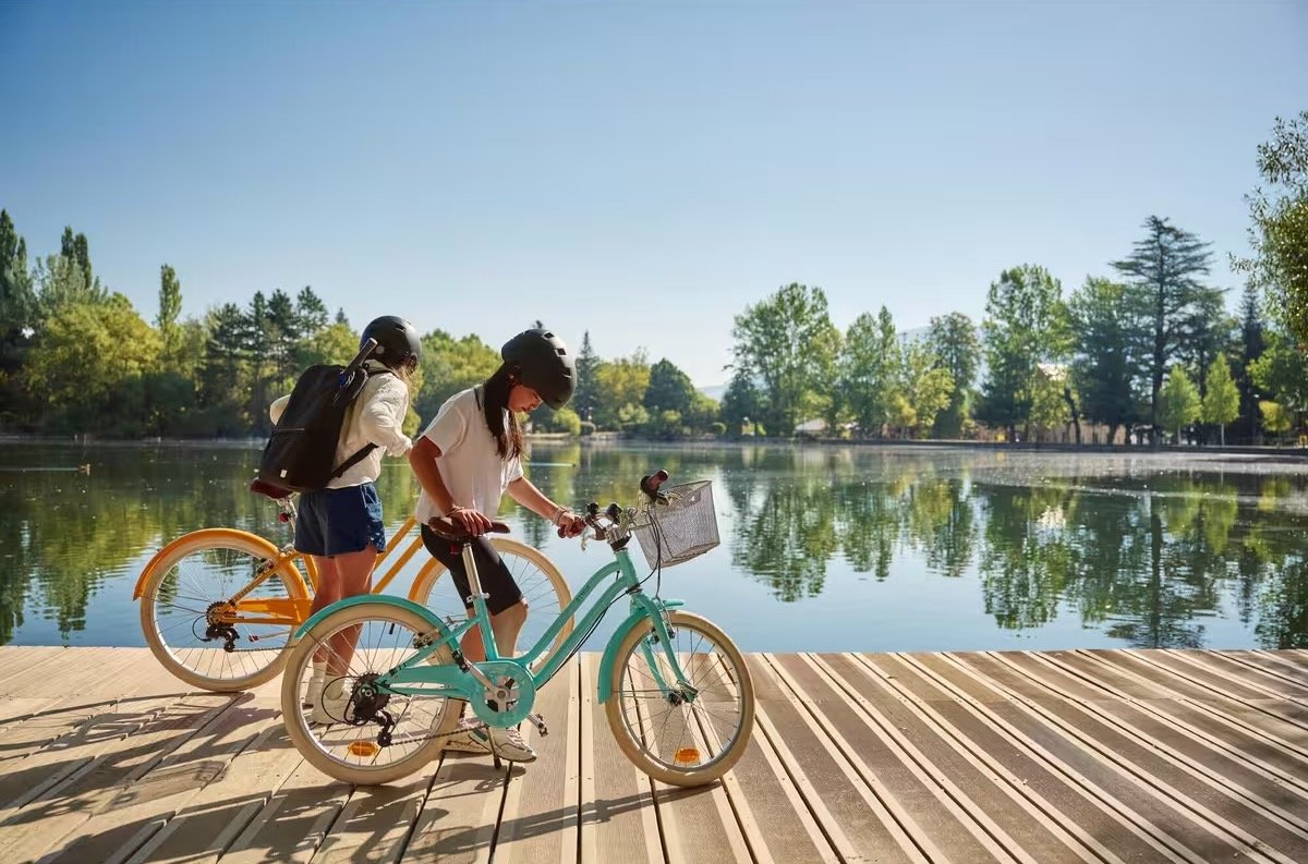 Deux filles avec des vélos de ville Btwin 500 de 20 pouces, cadre ouvert et panier, au bord d’un lac