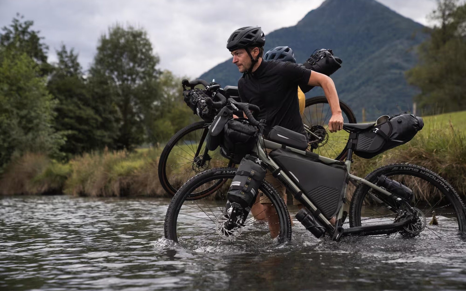 Cycliste équipé de sacoches Decathlon Riverside ADVT 900 en traversée de rivière lors d’un voyage à vélo en mode bikepacking.