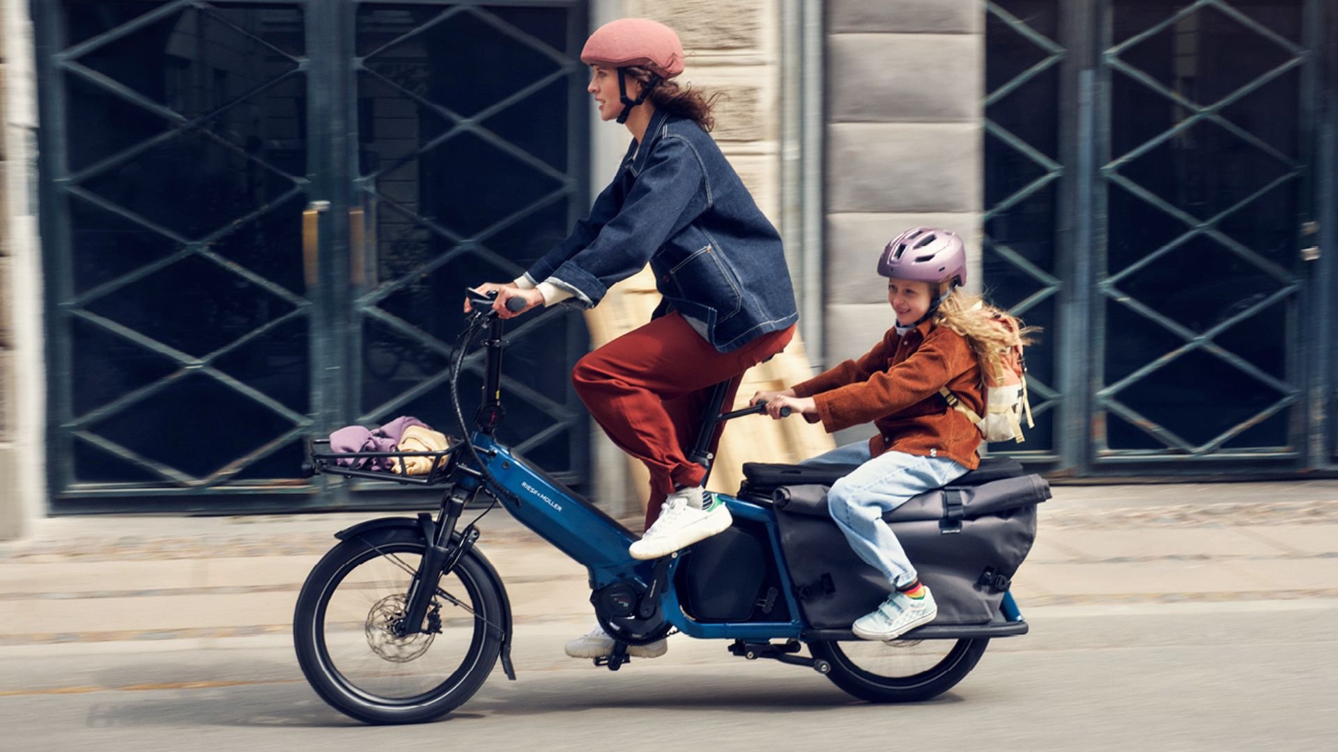 Femme et enfant sur un vélo cargo électrique Riese & Müller circulant en ville.