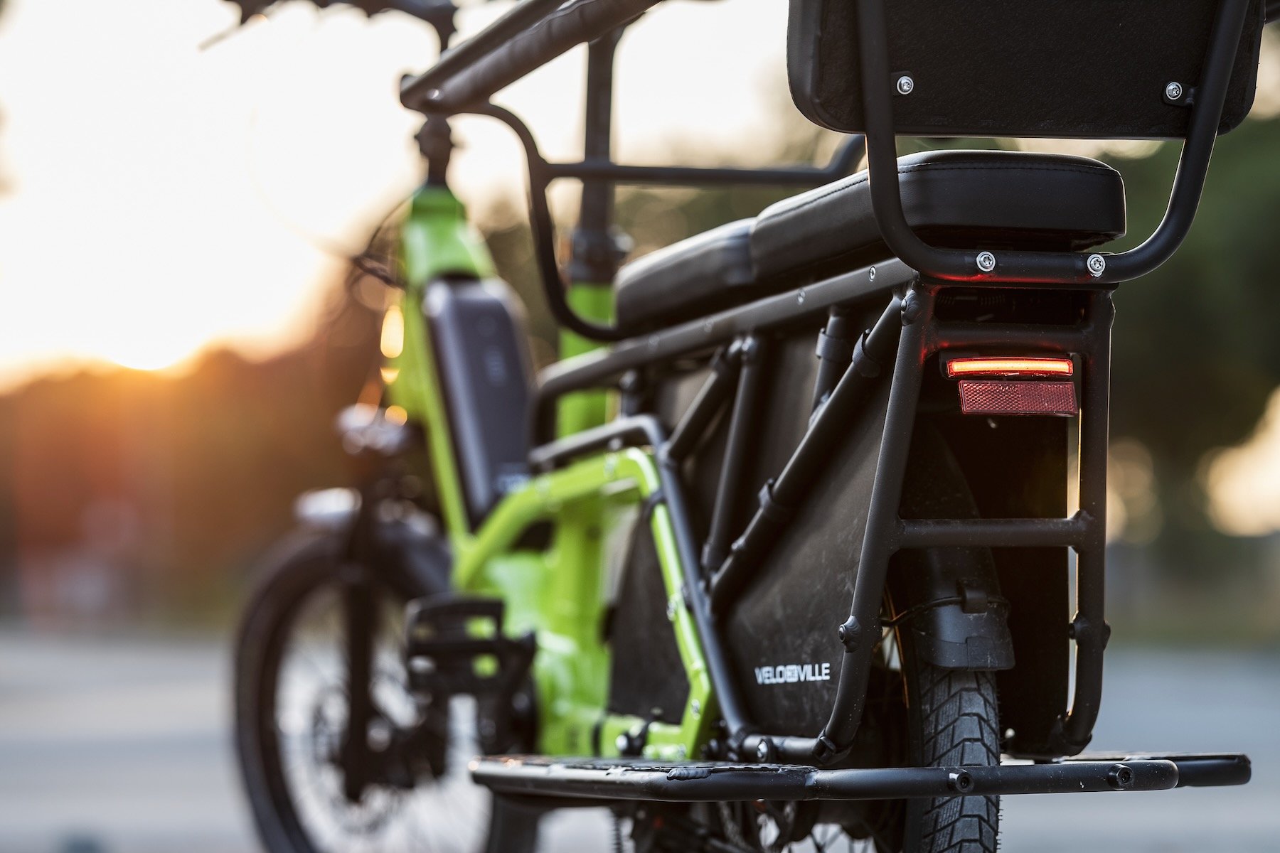 Gros plan arrière d'un vélo cargo électrique vert Velo de Ville avec porte-bagages et feu rouge allumé.