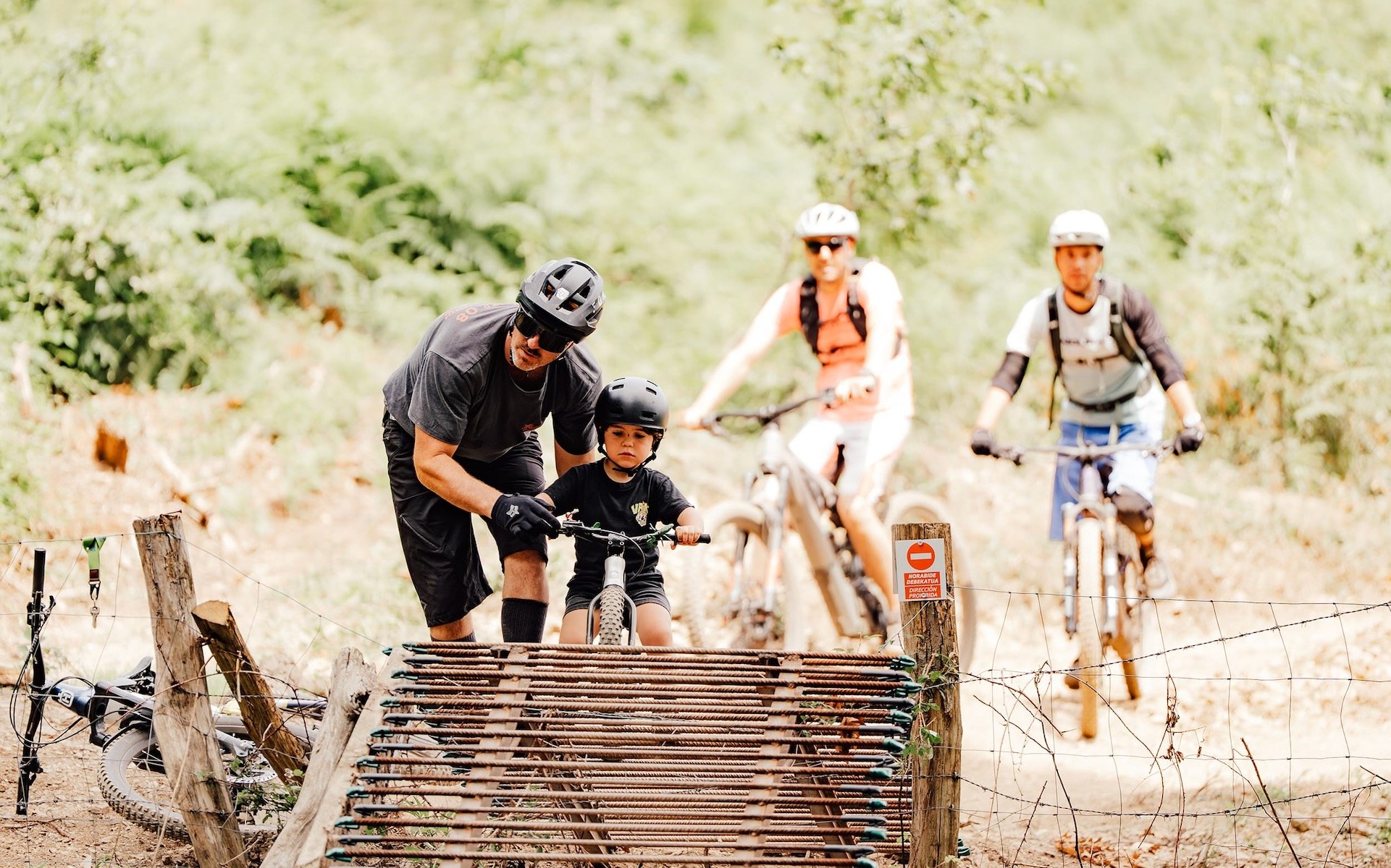 Un adulte aide un jeune enfant à vélo à franchir un passage sur un sentier de VTT forestier.