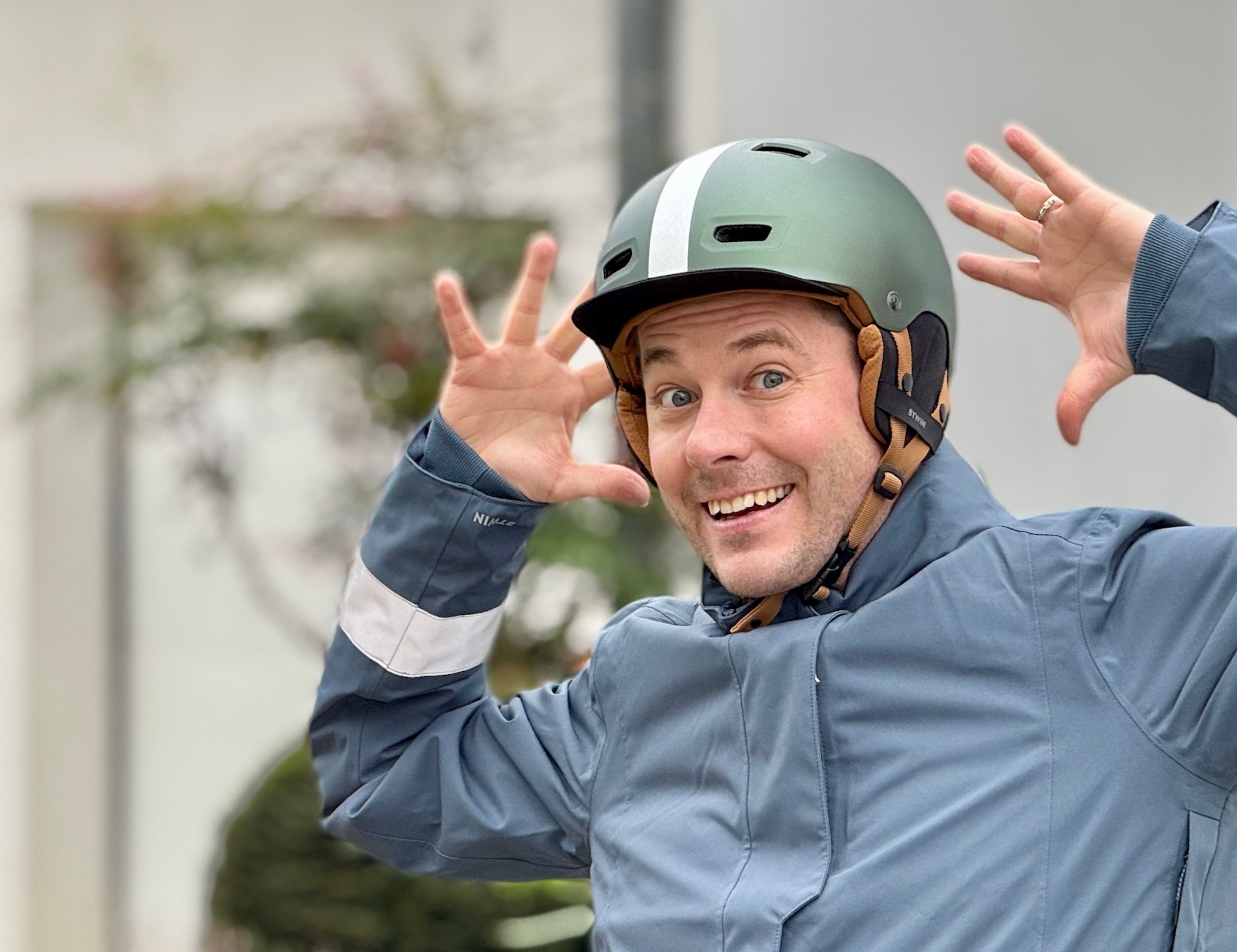 Homme souriant portant un casque de vélo vert et une veste de cyclisme bleue.