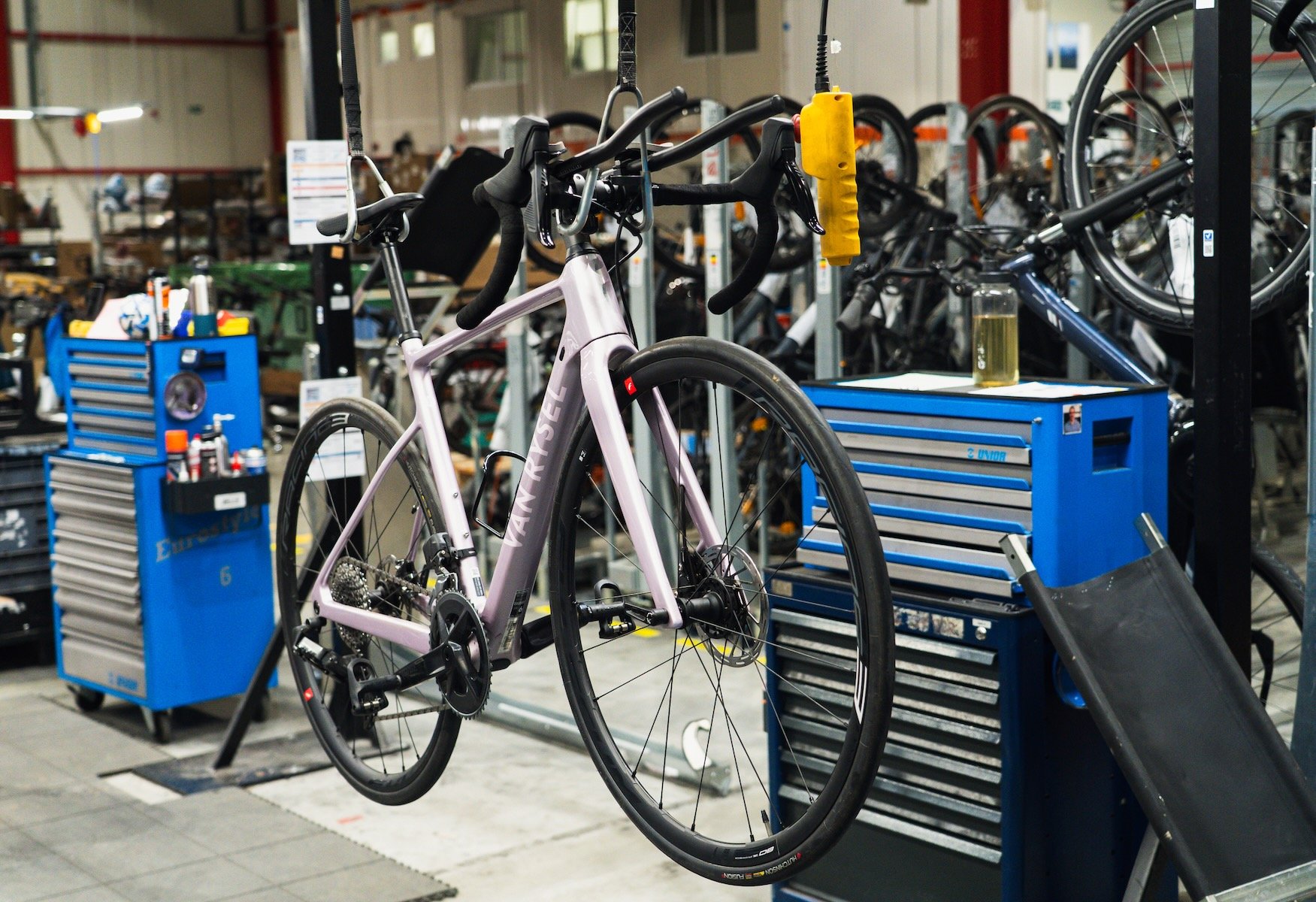 Vélo de route rose pâle suspendu dans un atelier de réparation Decathlon avec outils et autres vélos en arrière-plan