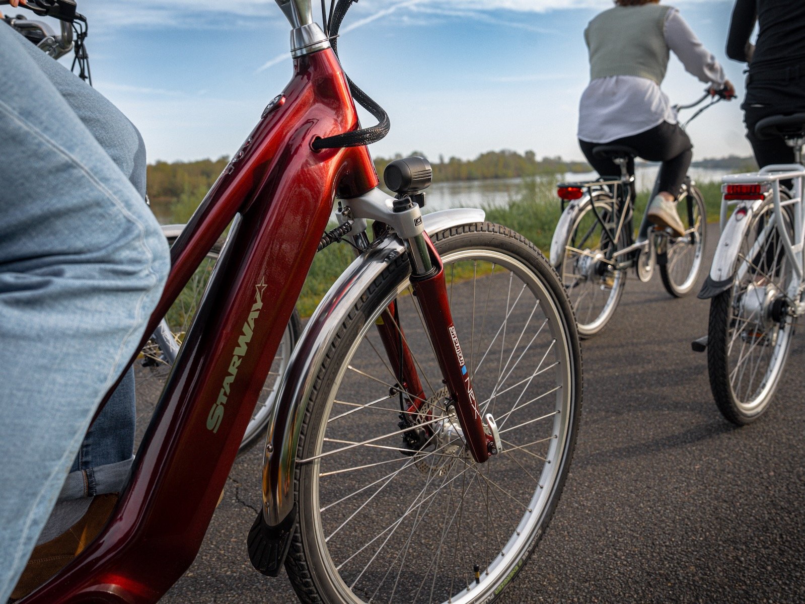 Vélo électrique Starway Touring GT rouge sur une voie verte en bord de rivière, suivi de deux cyclistes