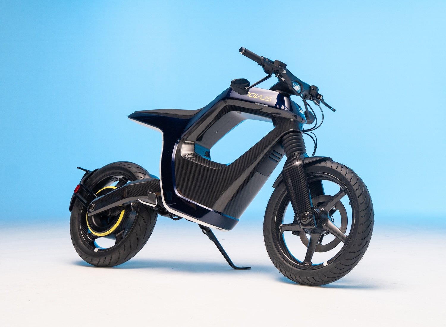 NOVUS One, deux-roues électrique noir à cadre en carbone ajouré, photographié en studio sur fond bleu