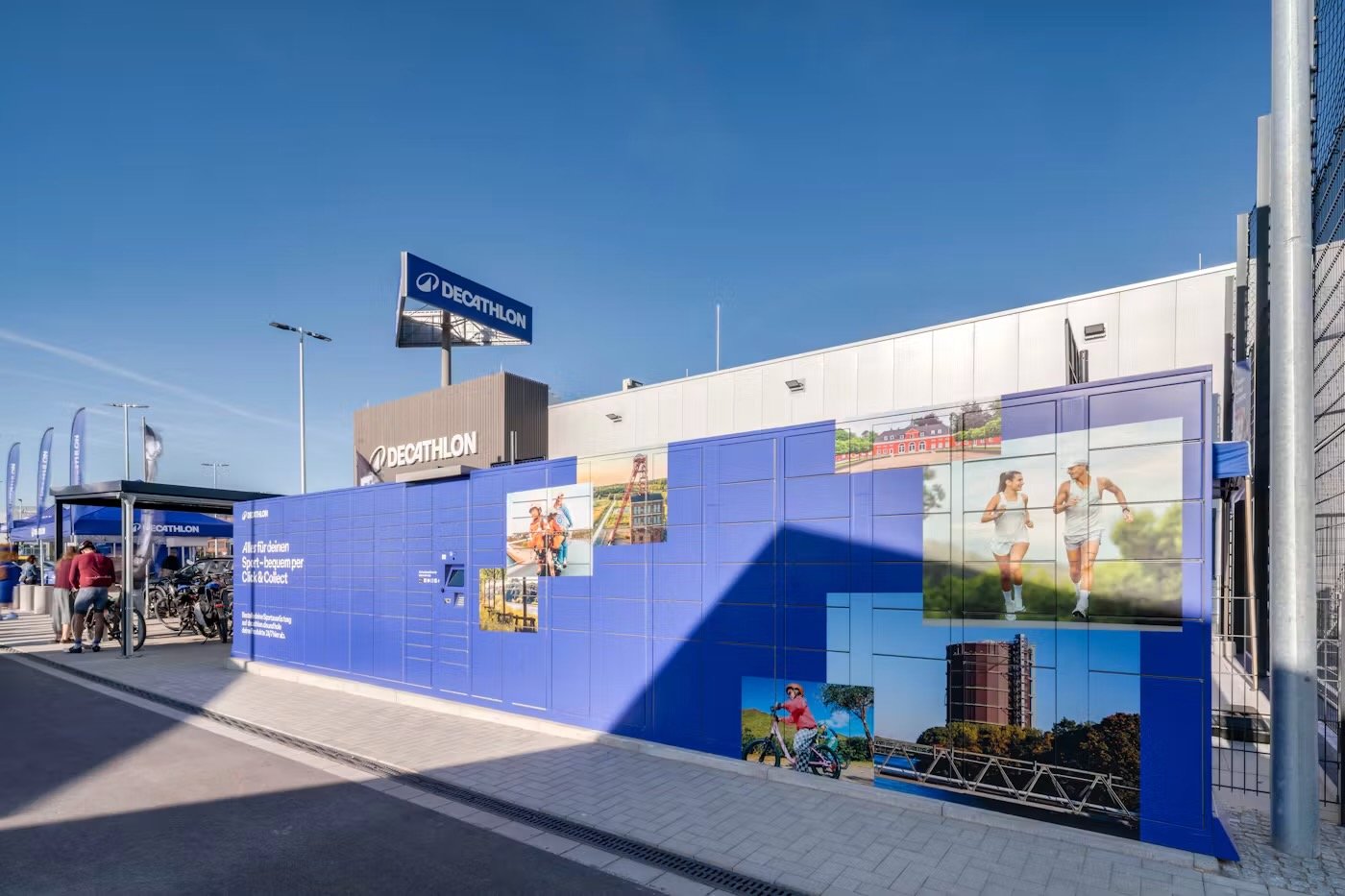Casiers Click & Collect bleus devant un magasin Decathlon en Allemagne, décorés de photos de sportifs et de paysages