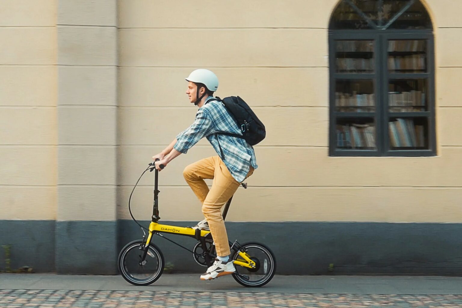 Cycliste en Dahon pliant jaune en ville, casque et sac à dos